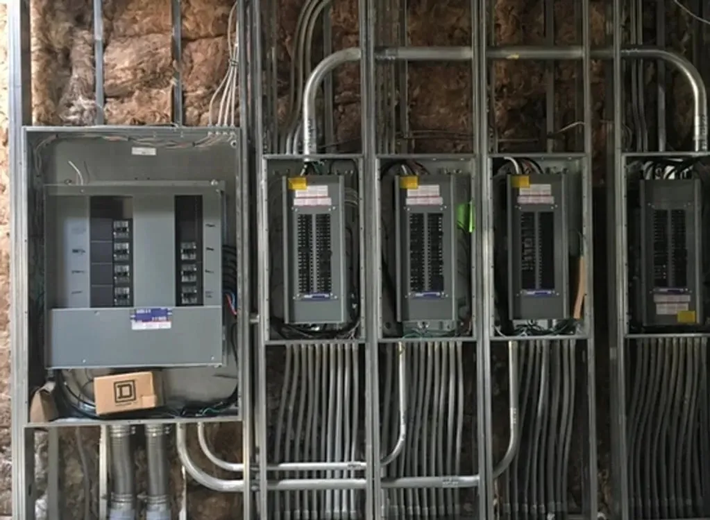 Row of commercial electrical panels and conduit runs mounted on a wall
