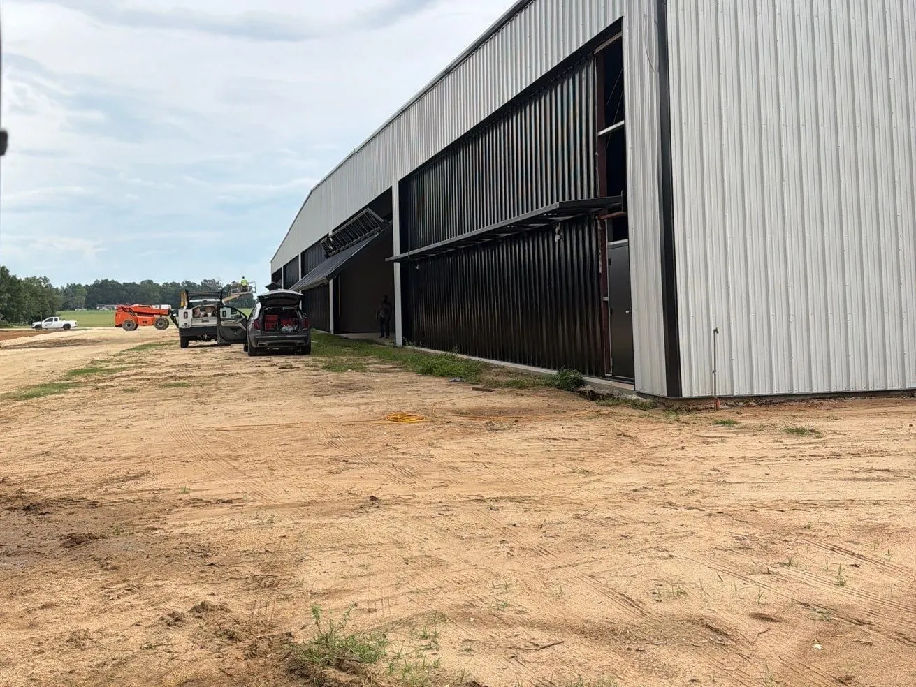 Row of new white steel hangars with dark hydraulic doors and a fresh concrete apron at Jumbolair