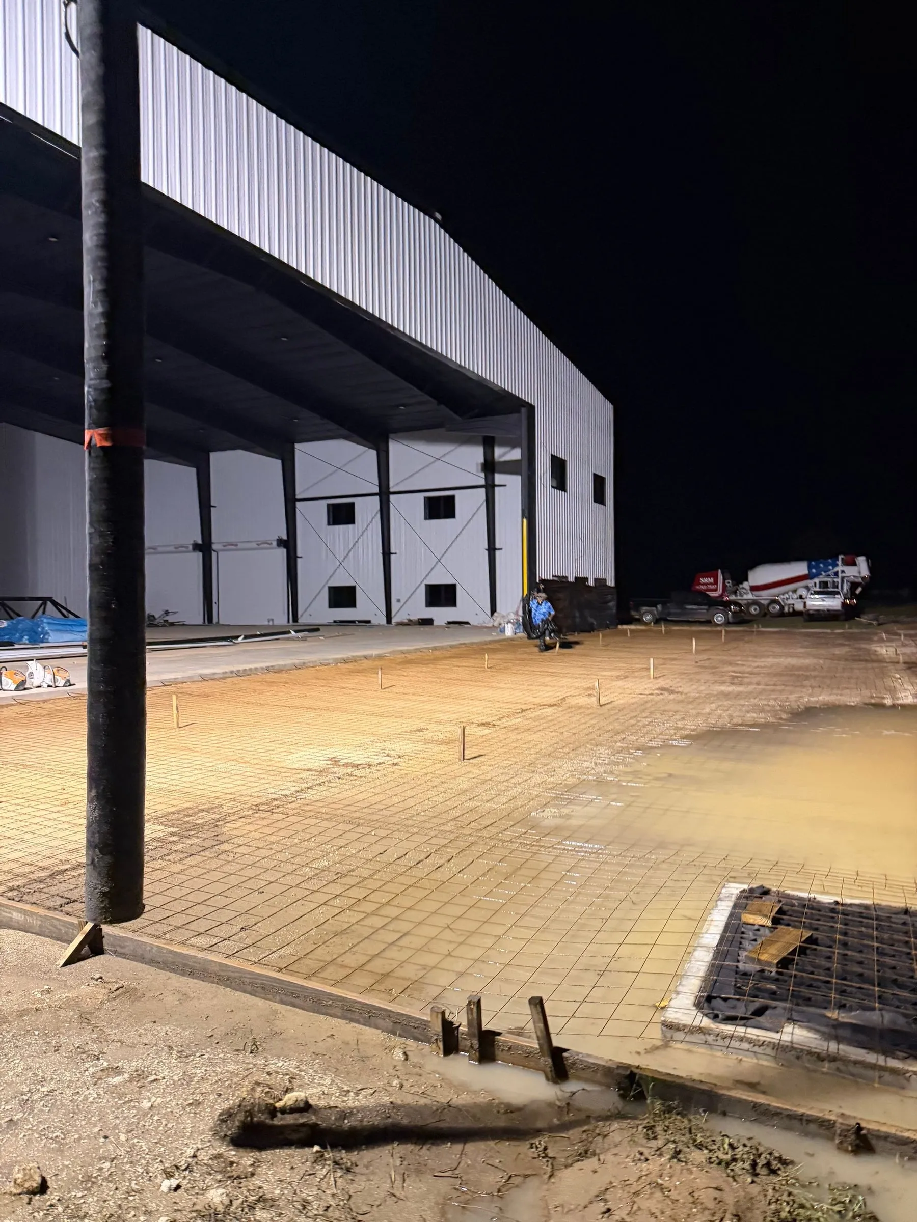 Concrete apron being poured in front of a hangar at night under work lights