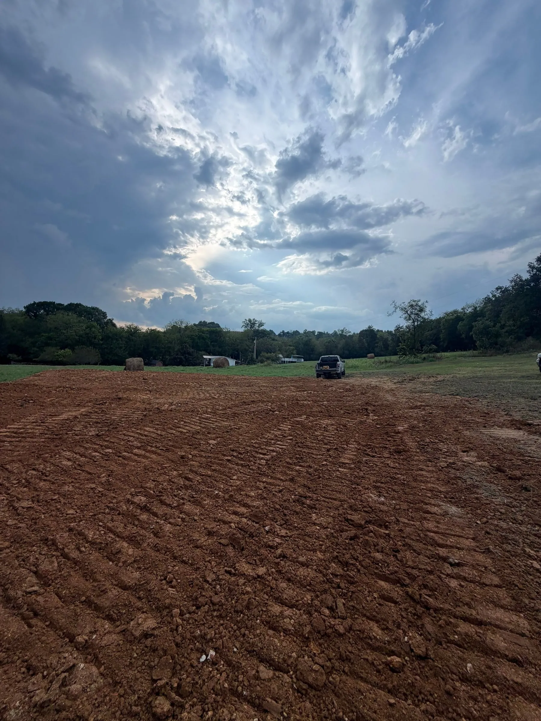 Freshly graded red-clay building pad under a dramatic sky