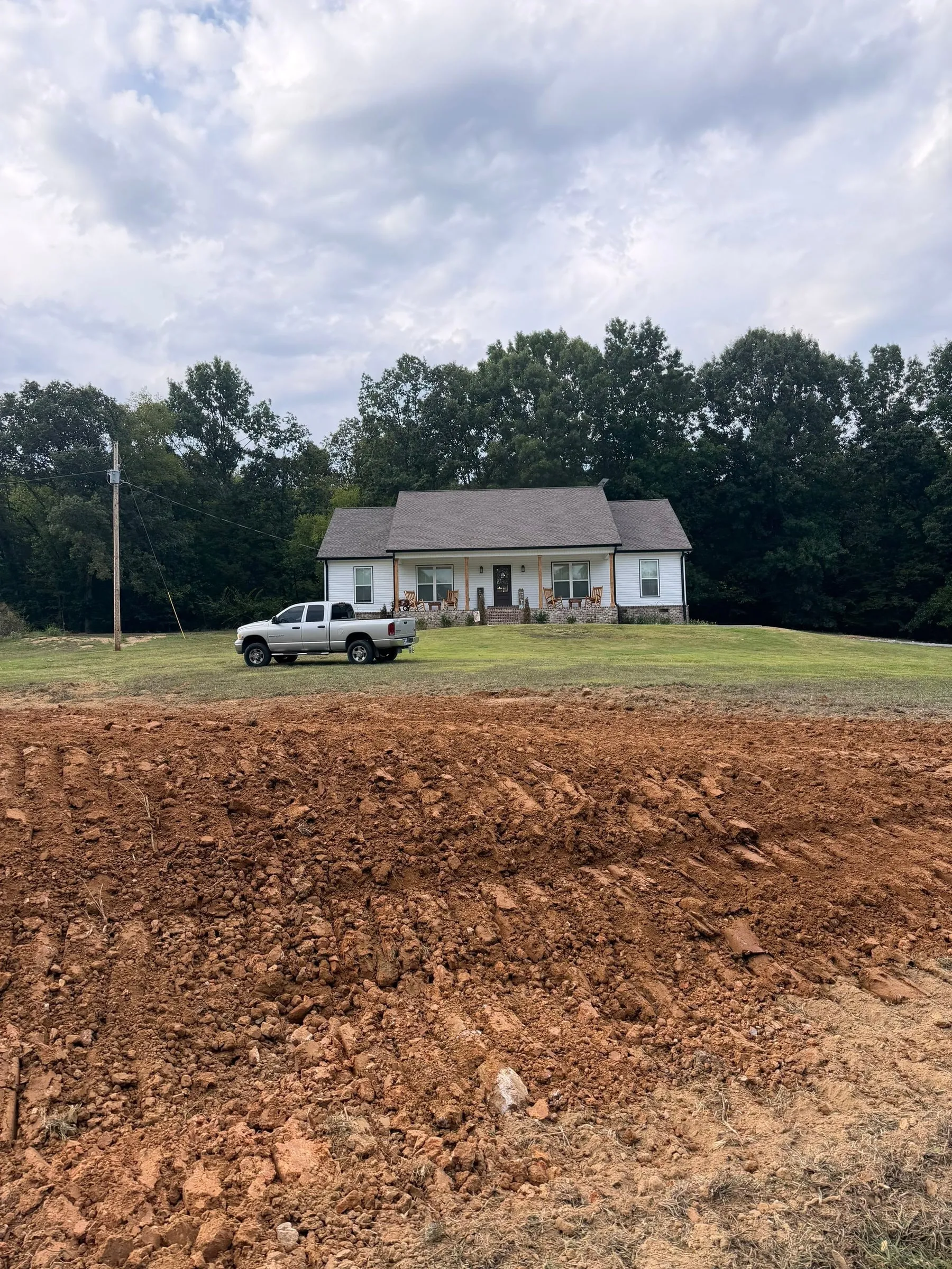 Wide view of the compacted pad with the house and tree line beyond