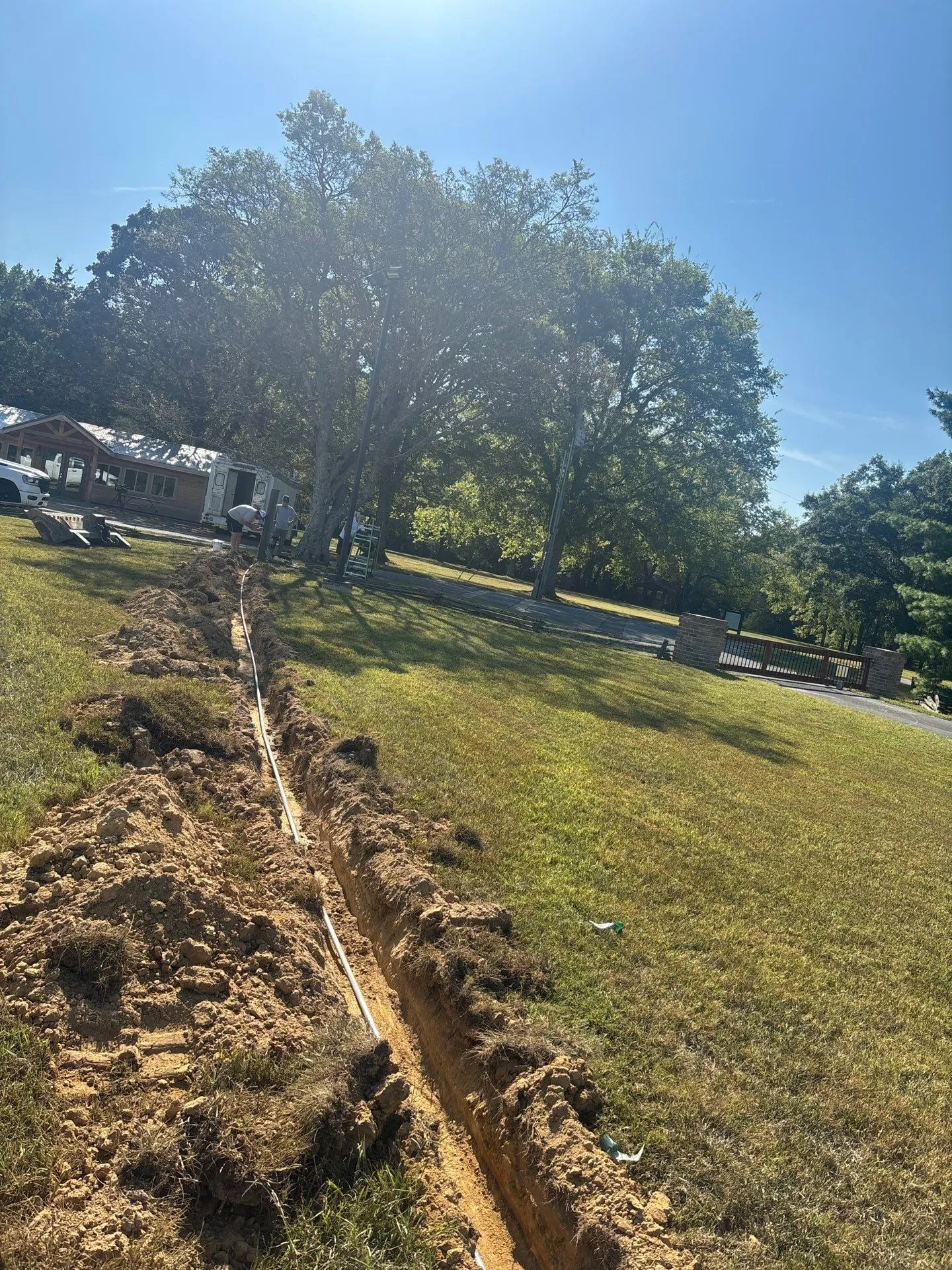 Trench for electrical feeders cut across a lawn between trees