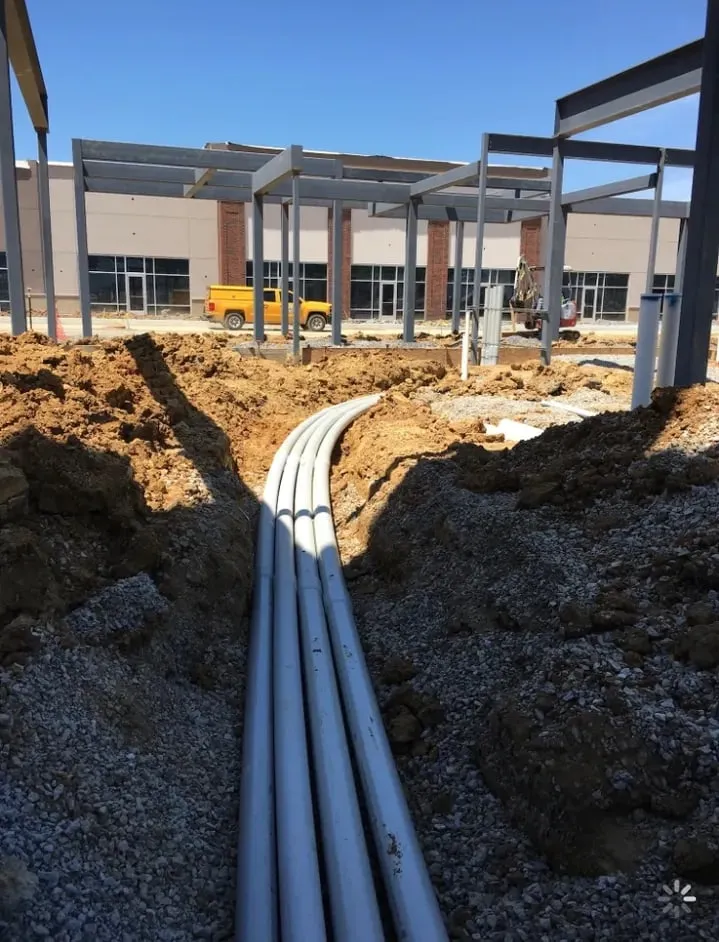 Underground conduit and pipe runs in an open trench beside steel building columns