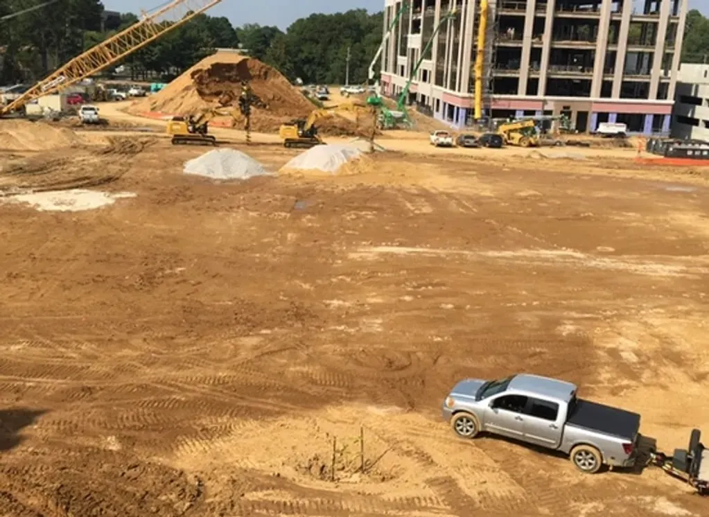 Excavators grading a large site with a commercial building under construction behind